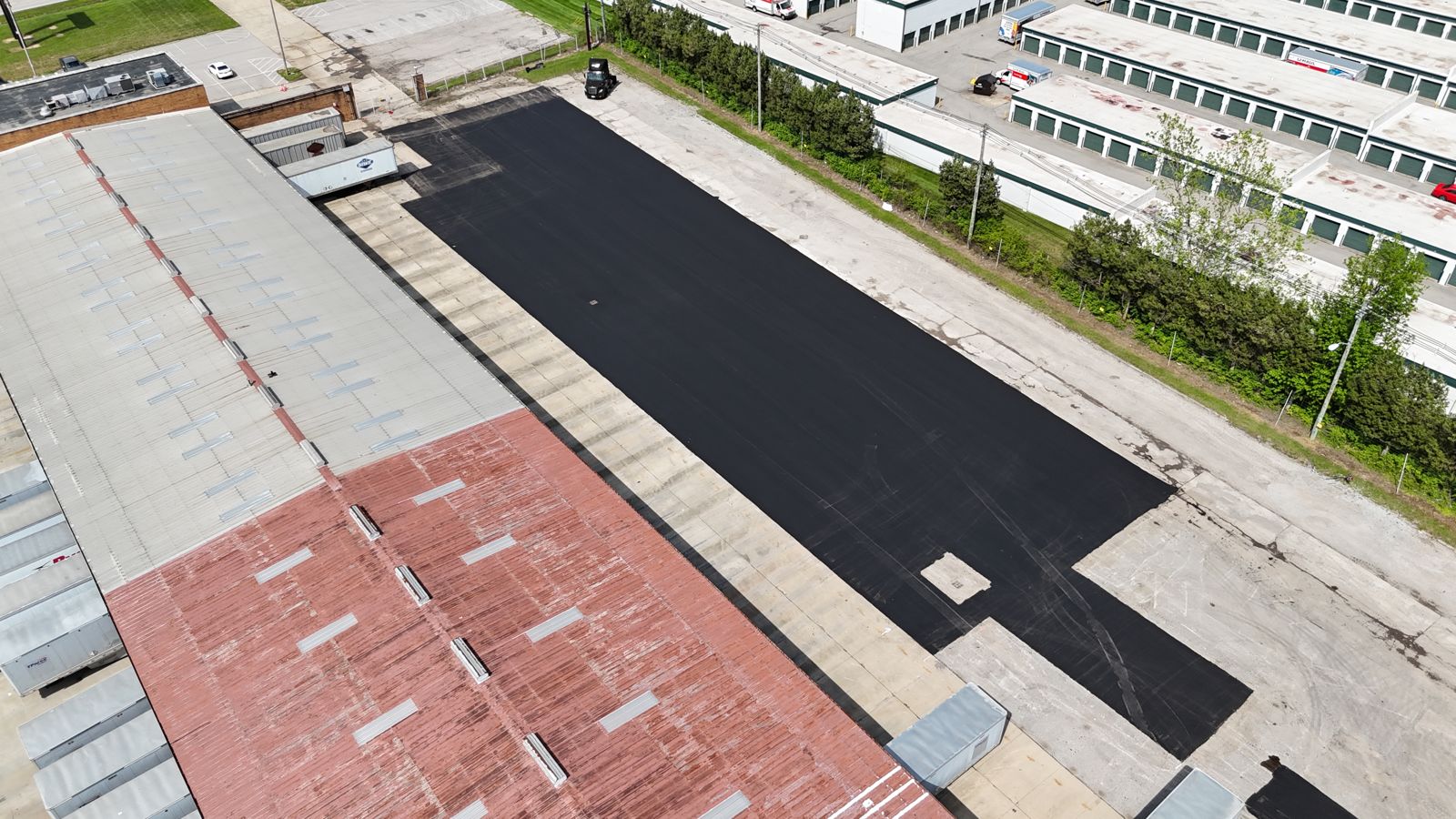 Top-down drone view of fresh black asphalt beside a building with a red roof