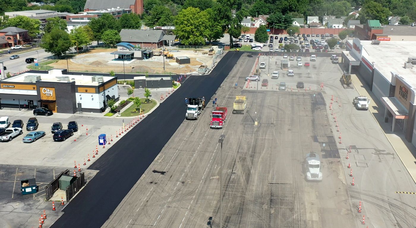 Drone view of a shopping center lot being paved, dump trucks laying fresh mat
