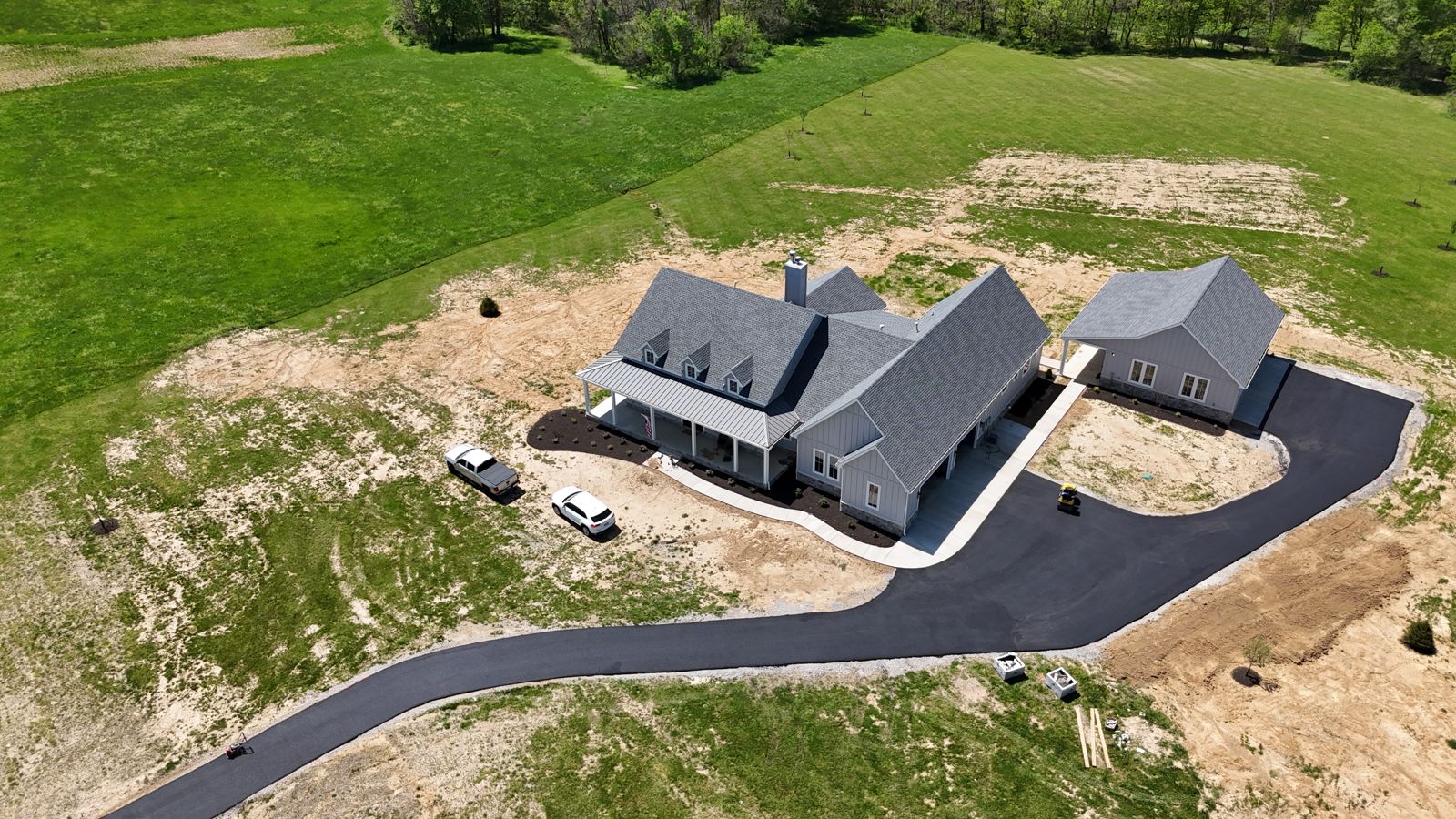 Drone view of a new home with a fresh asphalt driveway curving through bare ground