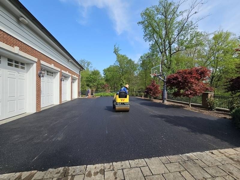Fresh asphalt driveway beside a brick garage, roller at work