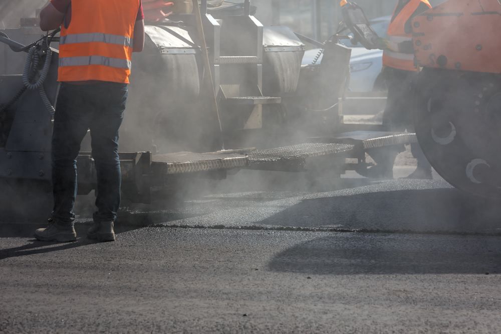 Paving crew working beside a paver in rising steam